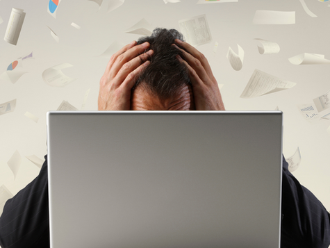 Um empresário ou dona de loja, sentado na frente do computador, olhando para o celular com cara de frustração.