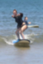 Smiling beginner surfer riding a small wave during a surf lesson in Tamarindo, Costa Rica.