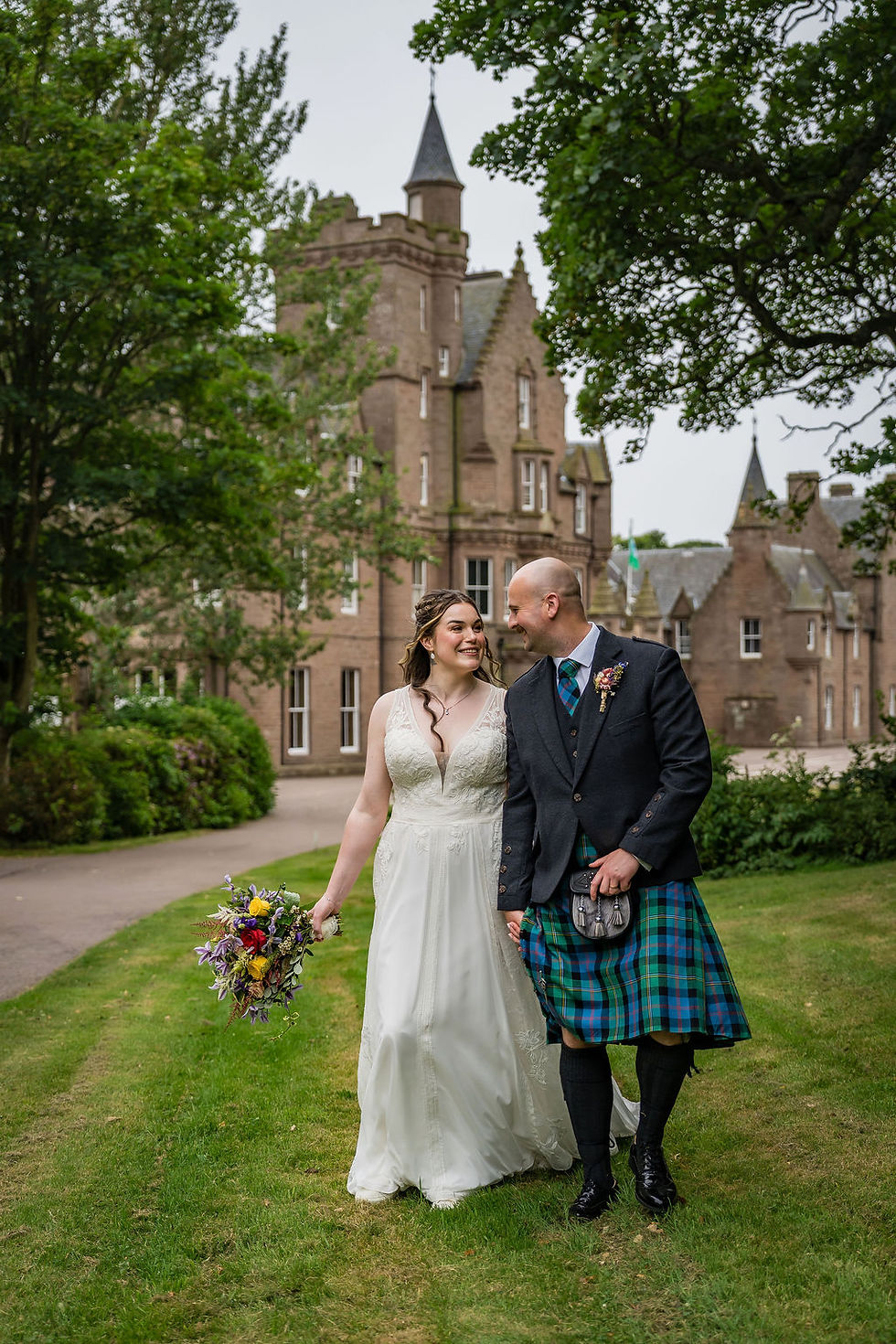 Bride and groom walking together in front of Brotherton Castle during their wedding couple portraits in Scotland.