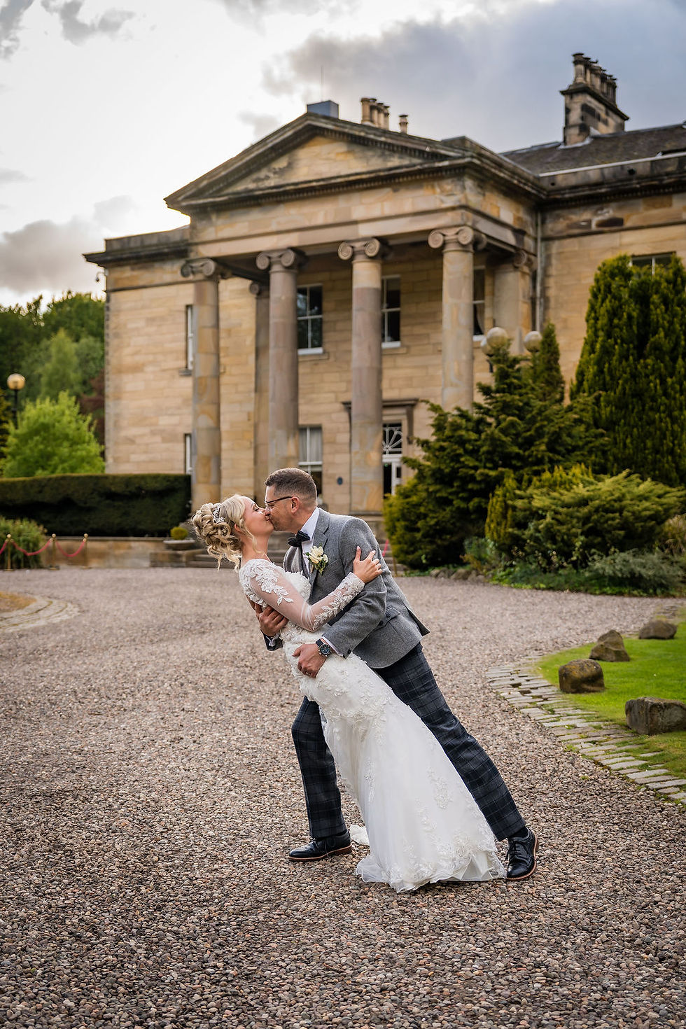 Bride and groom sharing dip kiss in front of Balbirnie House during romantic wedding portraits in Scotland