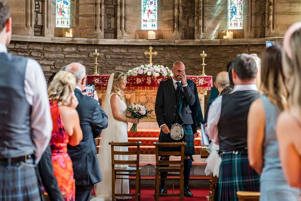 Wide shot of the groom laughing and crying with emotion during the wedding ceremony in a Scottish church