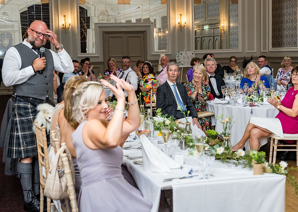 Wedding guests laugh while a bridesmaid excitedly raises her hands during the groom’s speech at Peebles Hydro—candid and joyful Scottish wedding photography.