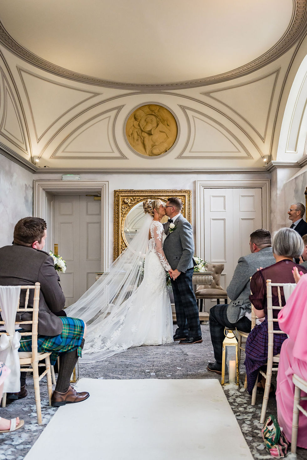 Bride and groom sharing first kiss after ceremony at Balbirnie House in Scotland surrounded by loved ones