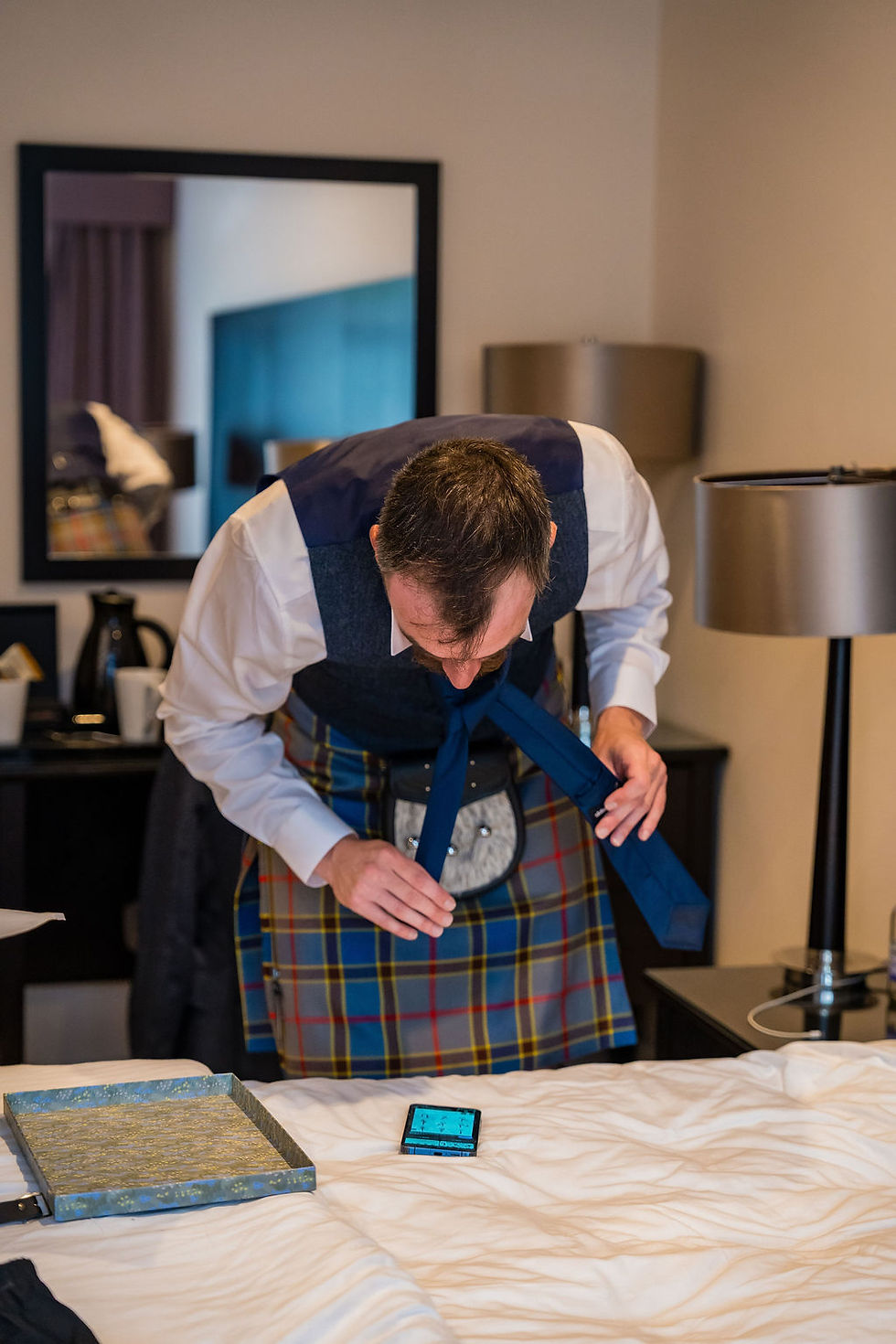 Best man watching a phone tutorial to learn how to tie his tie before the wedding, a fun morning moment with the groom.