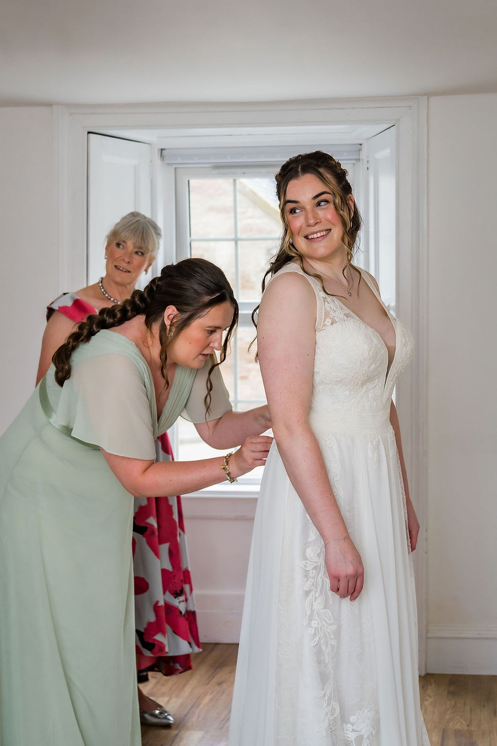 Bridesmaid helping the bride into her wedding dress during morning preparations.