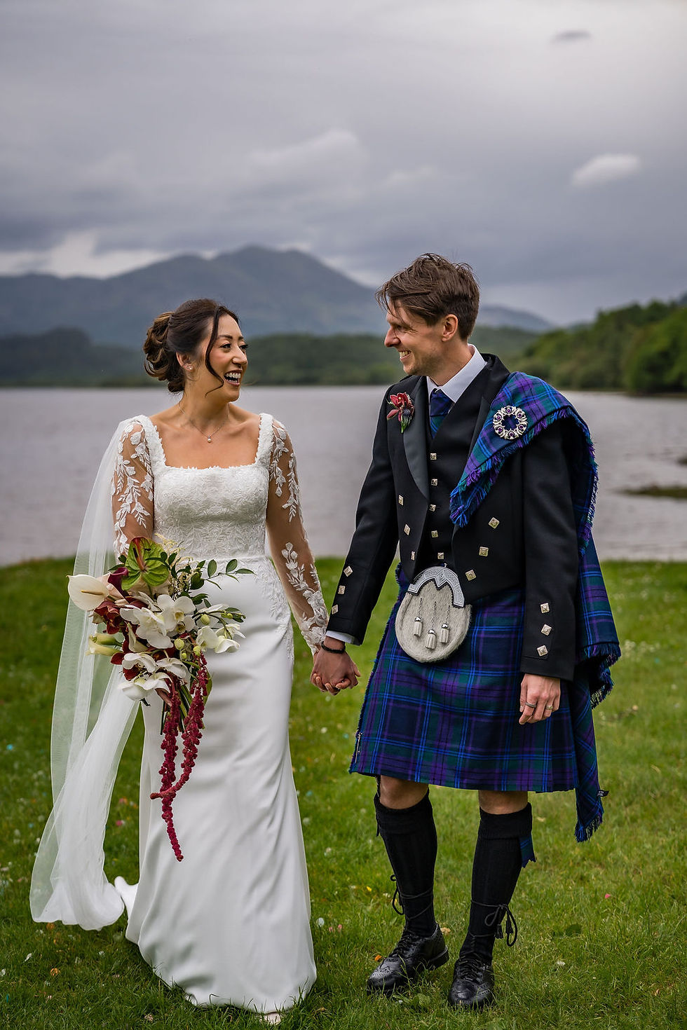 Bride and groom laughing together beside Loch Venachar during relaxed wedding portraits in Scotland