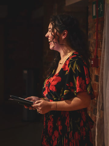 Smiling woman in floral dress, holding papers, laughing, stage background.