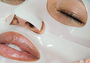 Close-up of a person's face wearing a white sheet mask, with closed eyes and glossy lips.