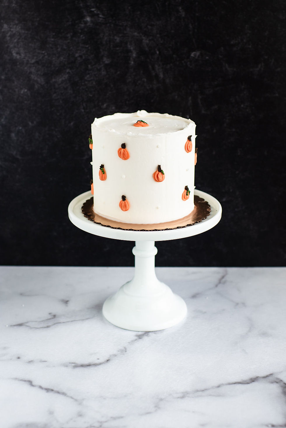 White buttercream fall cake decorated with small hand-piped orange pumpkin polka dots.
