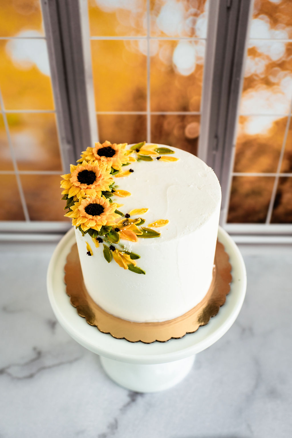 Fall sunflower cake with white buttercream, hand-piped golden sunflowers, dark centers, and cascading green buttercream leave