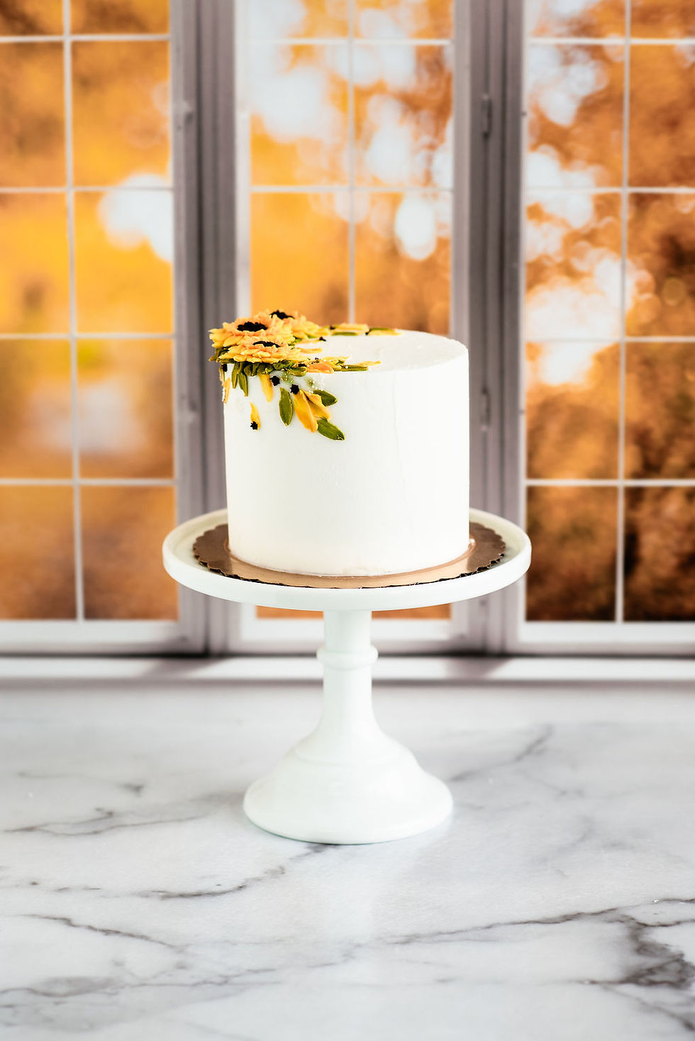 Fall sunflower cake with white buttercream, hand-piped golden sunflowers, dark centers, and cascading green buttercream leave