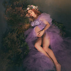 Dreamy pregnancy portrait of a woman lying on her side in a soft purple gown. Fine art style photography with cinematic lighting, evoking serenity and grace in a floral fairytale atmosphere.
