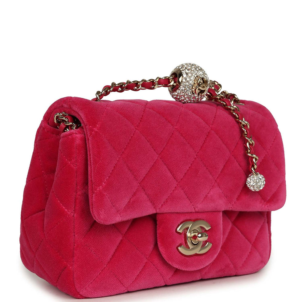 Three-quarter front view of the fuchsia velvet bag showing the crystal-set charm on the gold chain