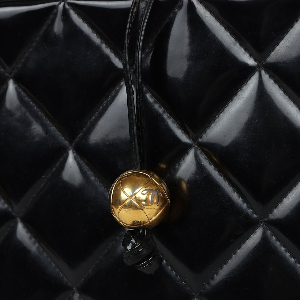 Thumbnail: Extreme close-up of the round gold-tone CC bead pull resting against the quilted panel