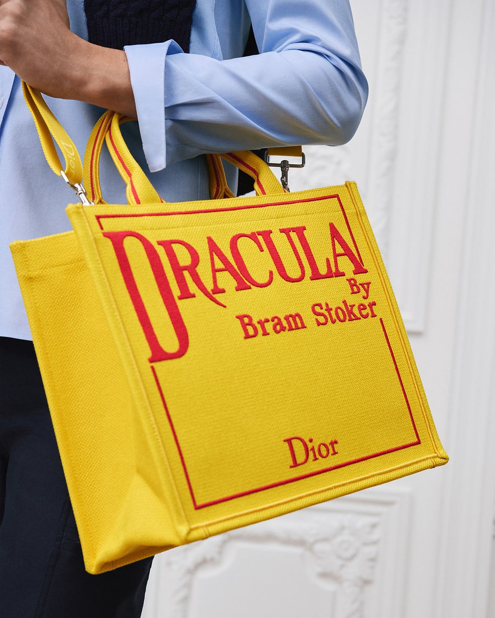 Thumbnail: Dior Medium Book Tote in yellow embroidered canvas with Dracula cover – carried by model, close-up