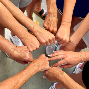 Multiple women's hands joined together to showcase their permanent jewelry.