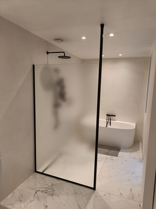 Maatwerk douchewand in Crepi figuurglas, afgewerkt met zwarte profielen en stabilisatiestang bevestigd in het plafond.