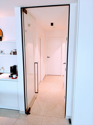 Plafondhoge pivoterende en zelfsluitende glazen deur in helder glas met kader in dagkant voor plinten.