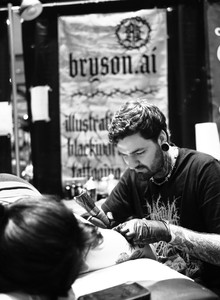 A black and white photo of a tattoo artist who is tattooing a person lying down.