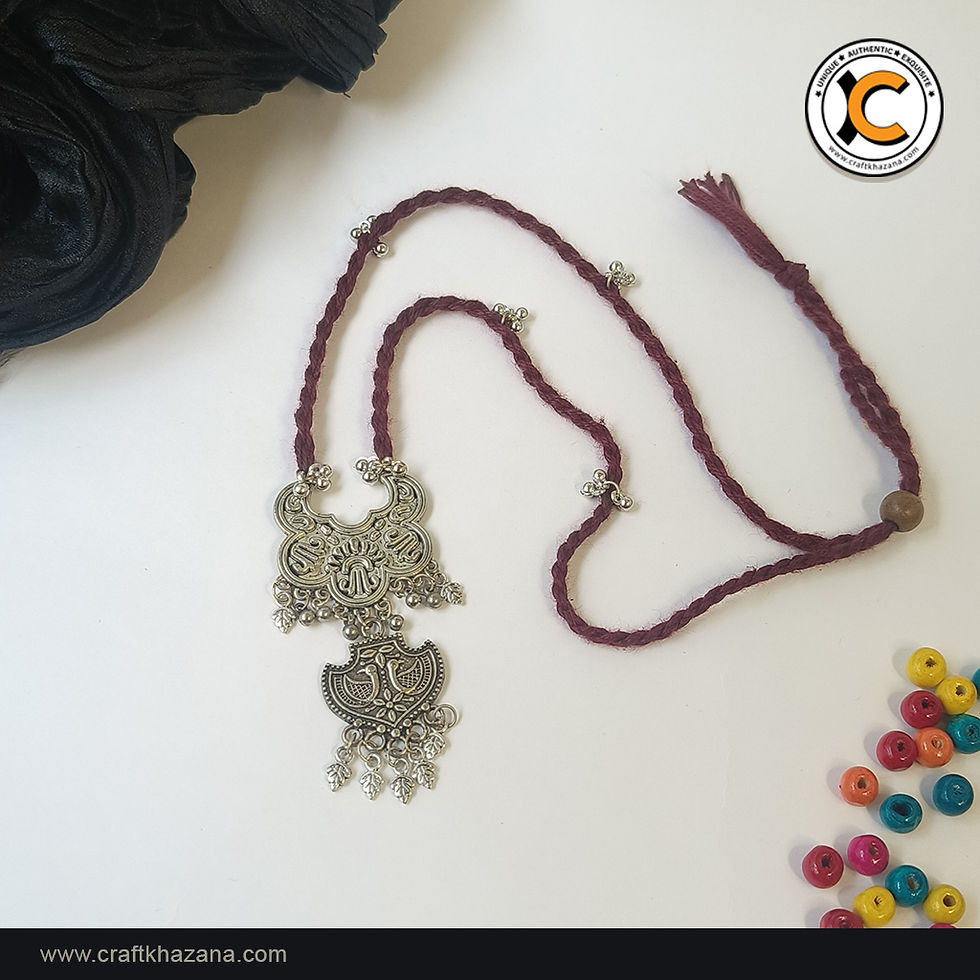 Maroon braided thread long necklace with oxidised silver double pendant, ghungroo bells and leaf charms, laid flat on a white