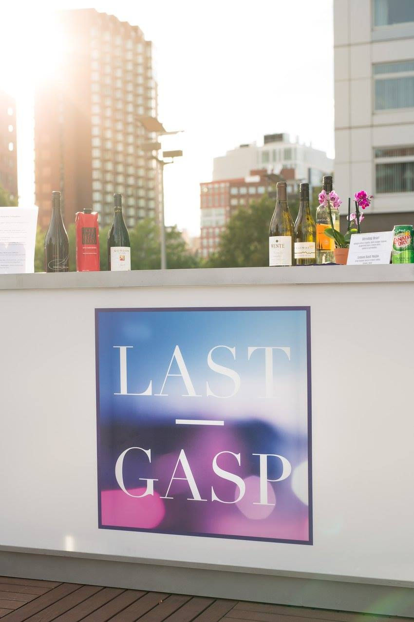 Bar with large illuminated Last Gasp logo set against Boston skyline at rooftop event.