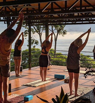 People practice yoga outdoors with raised arms, Costa Rica scenery, Tree Of India Yoga.