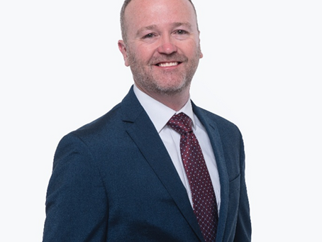 Professional corporate headshot of a smiling businessman wearing a navy-blue suit and burgundy patterned tie against a clean white background, photographed in Alpharetta, GA.