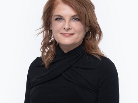 The picture is of a mature woman with auburn colored hair, and wearing a fashionable black top.
