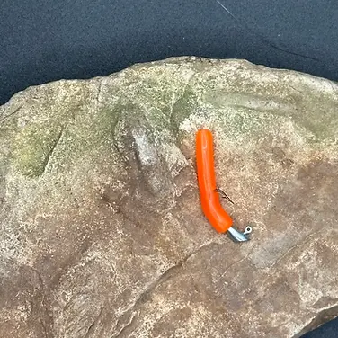 Round Trout Worm 2.95 inch soft plastic bait rigged on a jig head displayed on natural rock surface