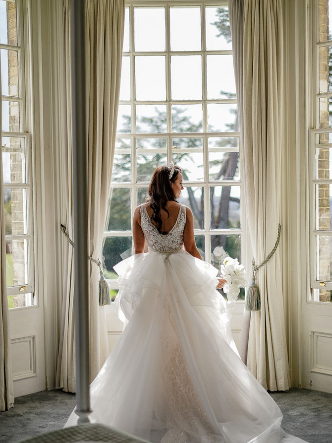 An elegant, cinematic bridal portrait taken at Hedsor House, capturing the bride in her wedding gown against the grand windows of the venue, by Reyweddings