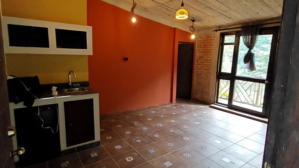 Interior de una casa vacía en colores blanco, rojo y amarillo, con acabados aparentes en muros de tabique y plafón de losa. Ventanal con vista al exterior con naturaleza.