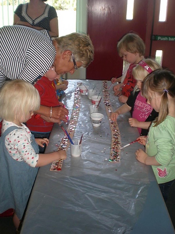 a teacher helping small children add sequins to a fabric border.