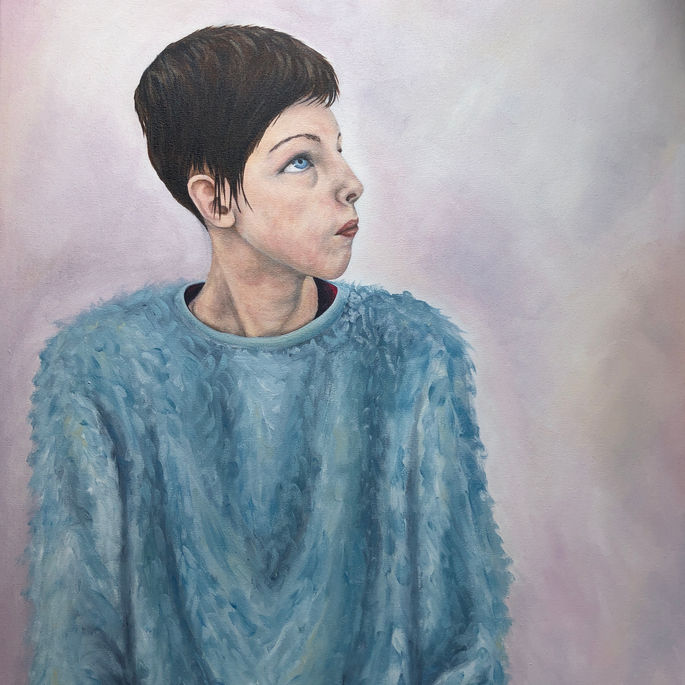 Portrait of a young girl looking to her right and up. She is wearing a blue jumper.