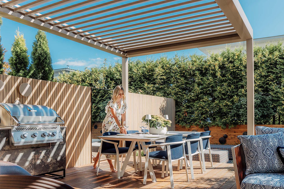 Stainless steel gas grill under a white louvred aluminium pergola beside a garden dining table