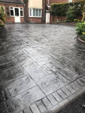 Slate grey pattern imprinted concrete driveway with brick edging.