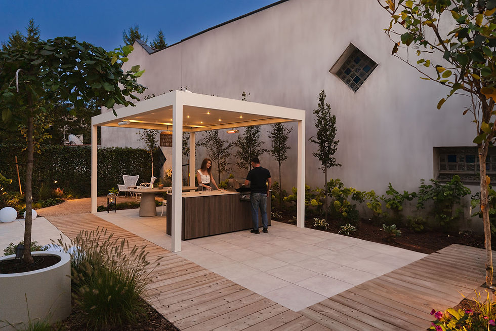 White aluminium pergola sheltering an outdoor kitchen island on a paved patio at dusk