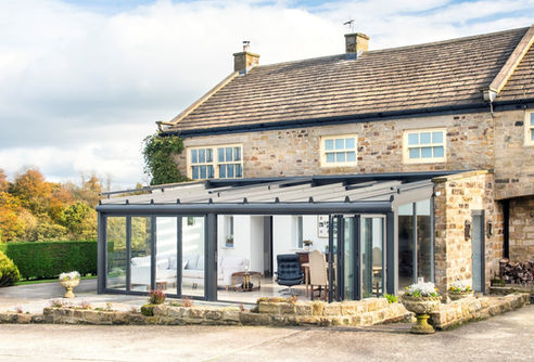 Modern glass winter garden extension with bi-fold doors on stone house.