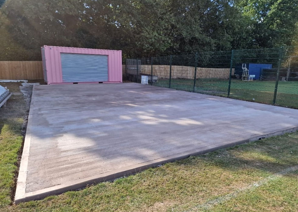 New concrete base slab laid on a fenced site beside a container