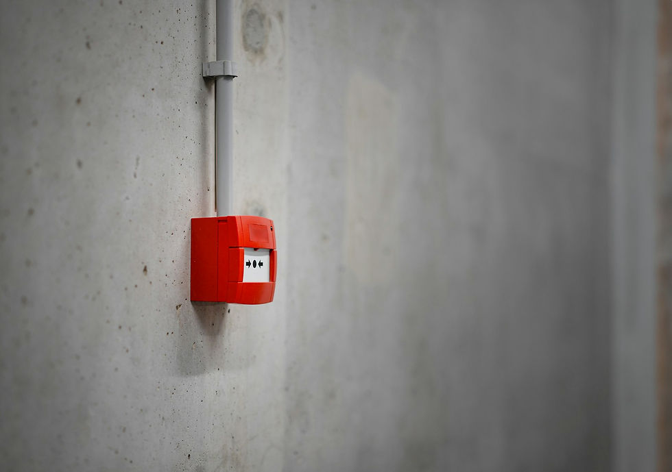 Red fire alarm call point fixed to a bare concrete wall below grey conduit