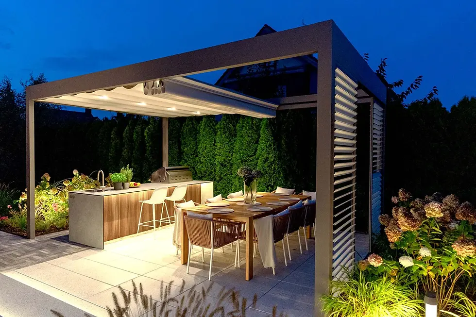 Freestanding bronze canopy pergola lit at night over an outdoor kitchen island and dining table