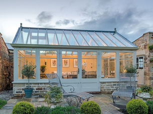Painted hardwood garden room with glazed roof and French doors in a stone courtyard at dusk