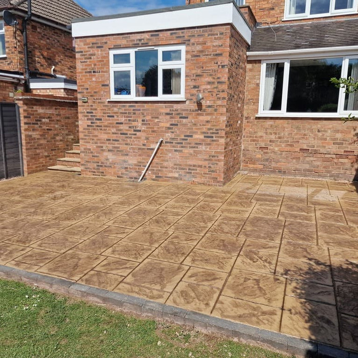 Buff pattern imprinted concrete patio outside a brick home.