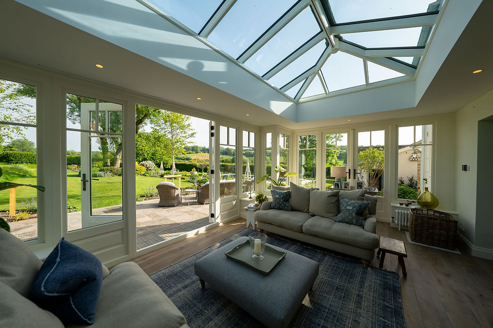 Orangery interior with a large white painted timber roof lantern, grey sofas and glazed doors open to a patio