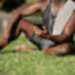 Close-up of a person wearing athletic clothes, sitting on bright green grass and looking at a smartphone. They have white wired earphones in and a gray towel draped over their shoulder.