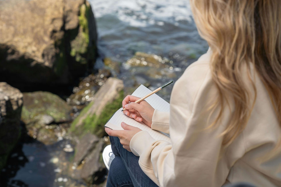ersona tomando notas en un cuaderno mientras se sienta frente al mar.