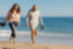 Mature couple walking barefoot along the beach shore.