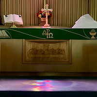 The altar under the light of the stained glass cross at the front of the church