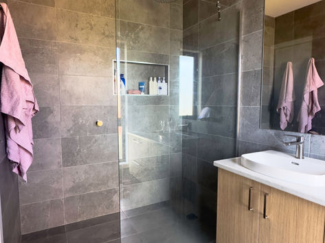 Ensuite with slate grey tiles, walk in shower with a rain shower head, wall hun floating vanity and pink accents