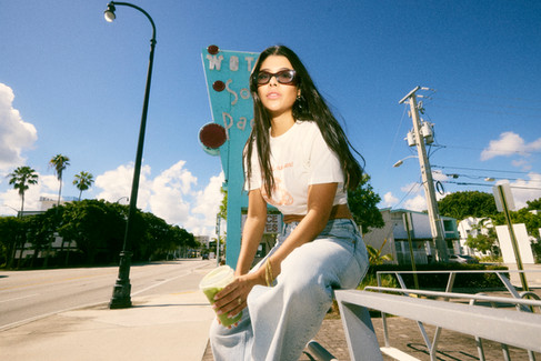Candid portrait of a woman in casual streetwear holding a Starbucks drink under the Miami sun, captured at the South Pacific Motel in lifestyle and street photography style.