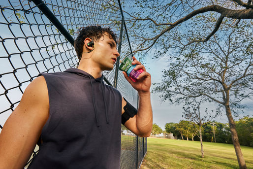 man drinking GoGo Squeez on a park with a fence behind